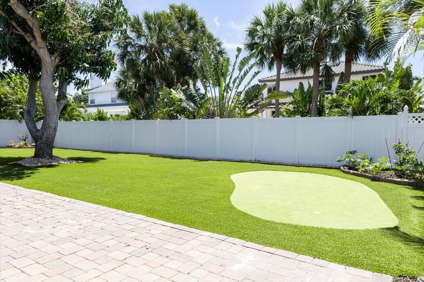 Lush backyard with synthetic putting green and palm trees, fenced for privacy.
